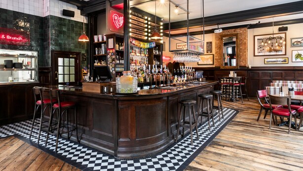 A bar area with a checkered floor, wooden bar counter, and stools.