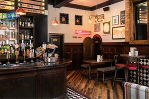 Zona de bar con mostrador de madera, estantes con botellas y un letrero de neón.