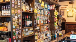 A bar area with shelves stocked with various bottles and snacks, a neon sign, and a coffee machine.