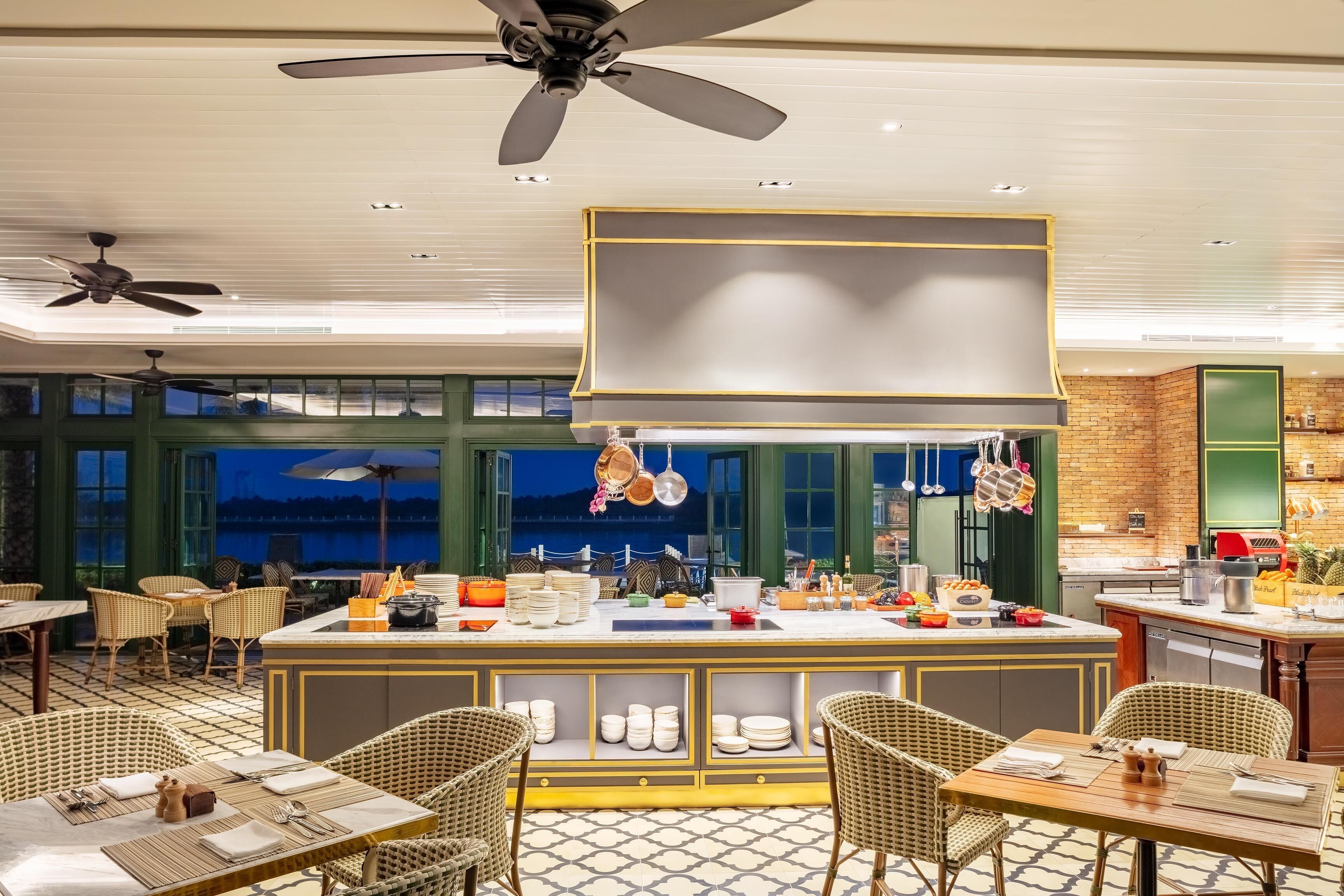 Een restaurant met een centraal gelegen bar, rieten meubilair en uitzicht op de stad 's avonds.