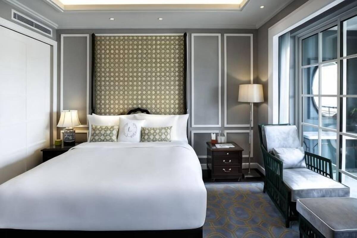 Une chambre d’hôtel avec un grand lit, des tables de chevet, une chaise, une fenêtre et une vue sur l’extérieur.