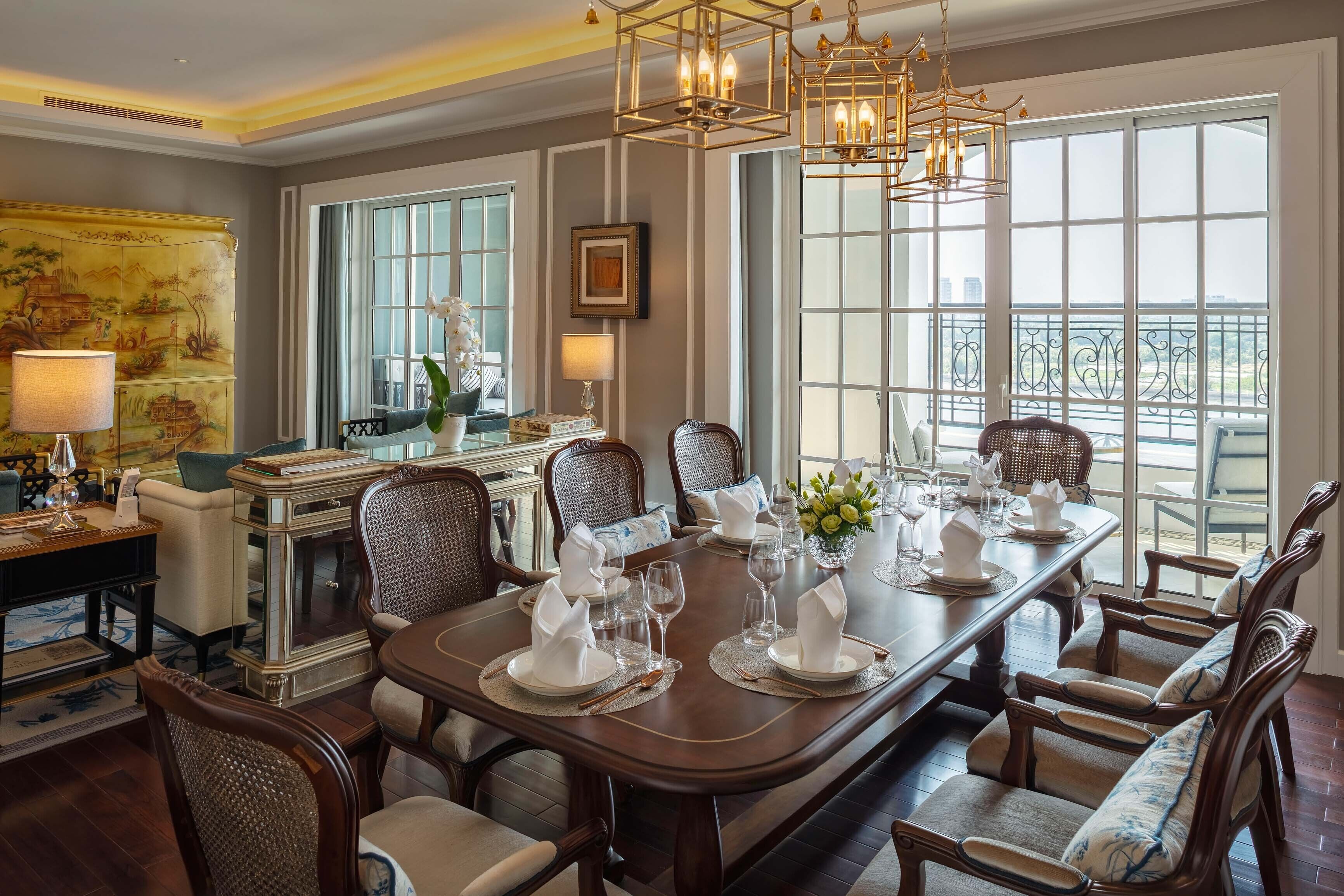 Un comedor formal con una larga mesa dispuesta para una comida, ventanas amplias con vistas y muebles clásicos.
