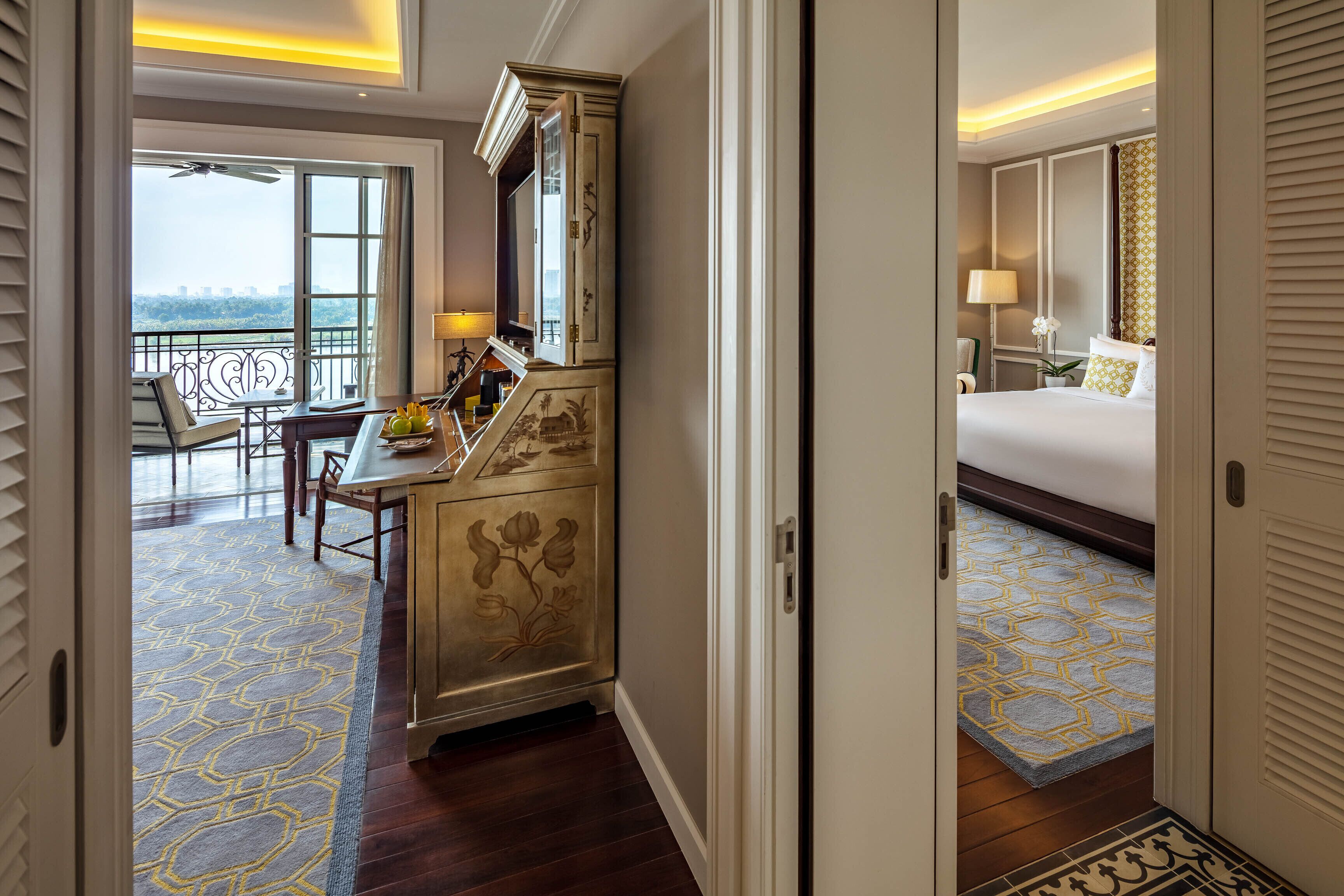 Une chambre d’hôtel avec un balcon, un bureau avec une chaise, un lit avec un tapis à motifs et un meuble décoratif.