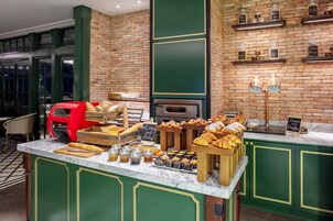Mostrador de panadería con diversos pasteles y pan, una máquina para gofres roja y estantes con frascos etiquetados con ingredientes.