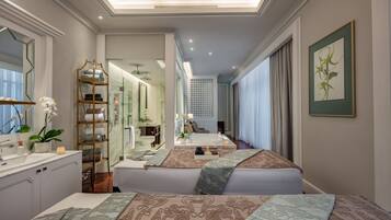 A hotel room with a large bed, a sitting area, a bathroom with a glass shower, and a view of the city.