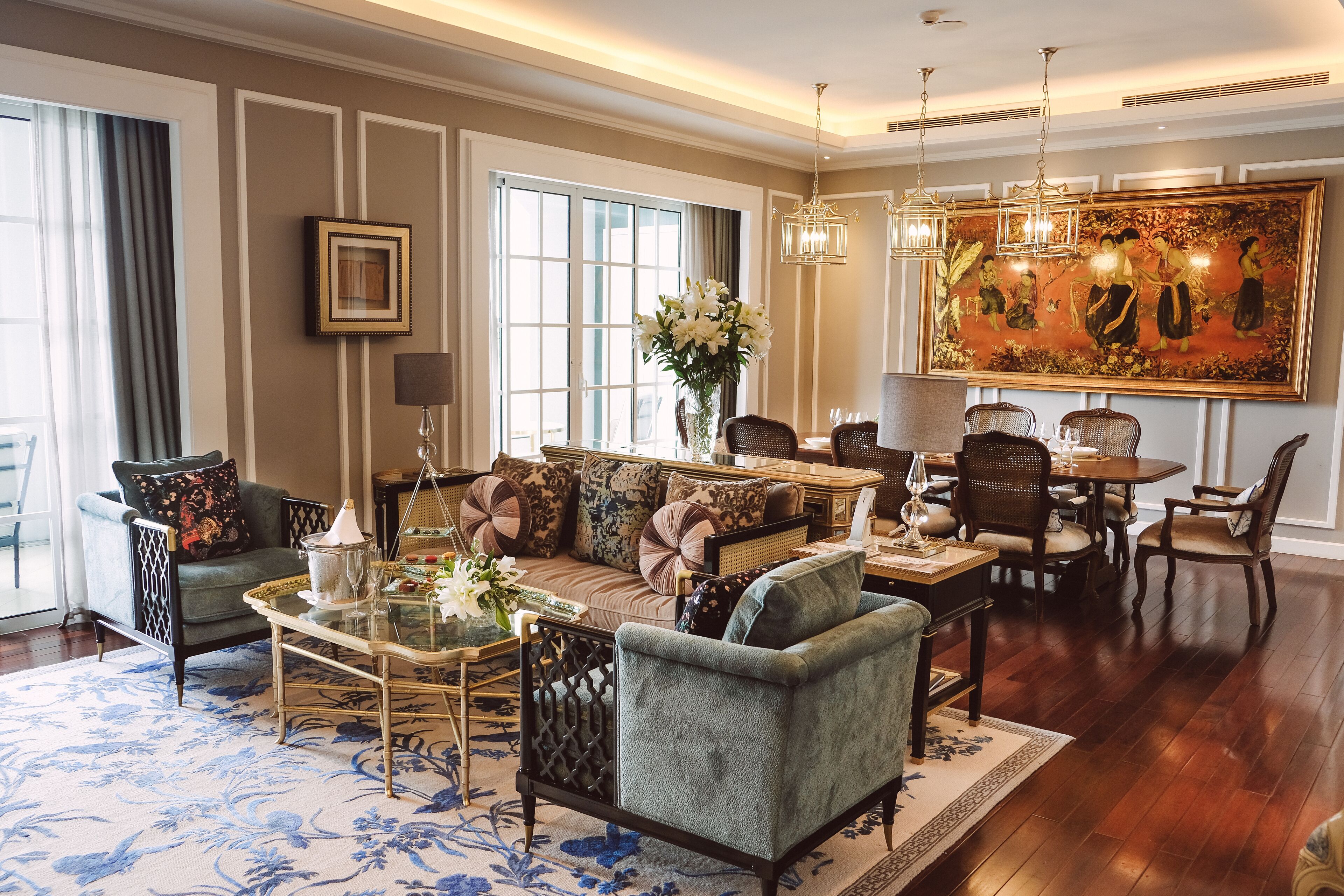 A spacious living room with a sofa, chairs, a coffee table, and a dining area with a chandelier and a large painting on the wall.