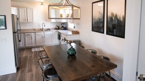 A modern kitchen with white cabinets, a wooden dining table, and a hanging light fixture.