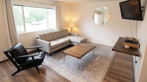 A modern living room with a sofa, a coffee table, a black leather chair, a TV, and a lamp.