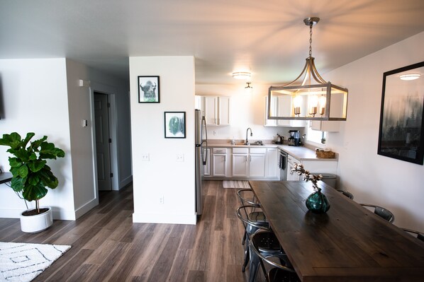 Una cocina moderna con armarios blancos, una mesa de comedor de madera y una lámpara colgante.
