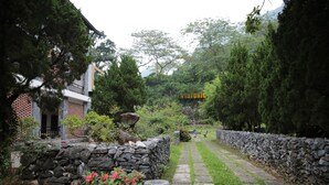 A stone pathway leading through a garden with a stone wall on one side and a building with a balcony on the other. - Historic Eco House & Ha Giang Loop (Ha Giang 2)
