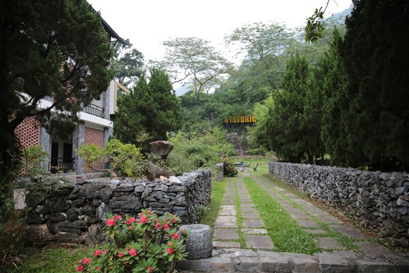 A stone pathway leading through a garden with a stone wall on one side and a building with a balcony on the other. - Historic Eco House & Ha Giang Loop (Ha Giang 2)