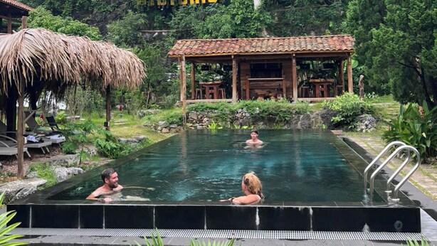 An outdoor swimming pool with a wooden structure in the background, surrounded by lush greenery. - Historic Eco House & Ha Giang Loop (Ha Giang 2)