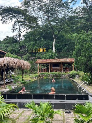 An outdoor swimming pool with a wooden structure in the background, surrounded by lush greenery. - Historic Eco House & Ha Giang Loop (Ha Giang 2)