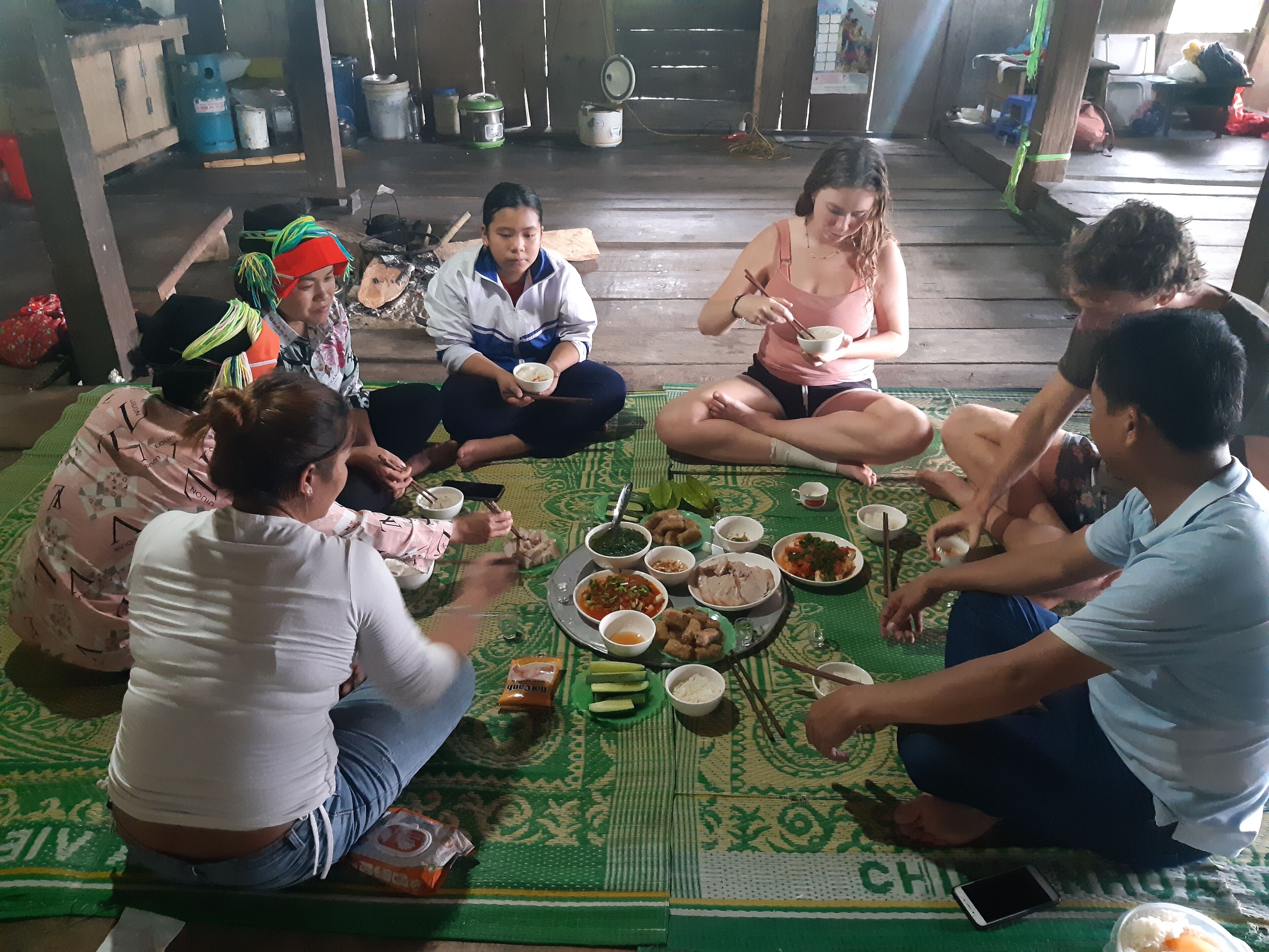 Un grupo de personas sentadas sobre una estera, compartiendo una comida con varios platos frente a ellas.