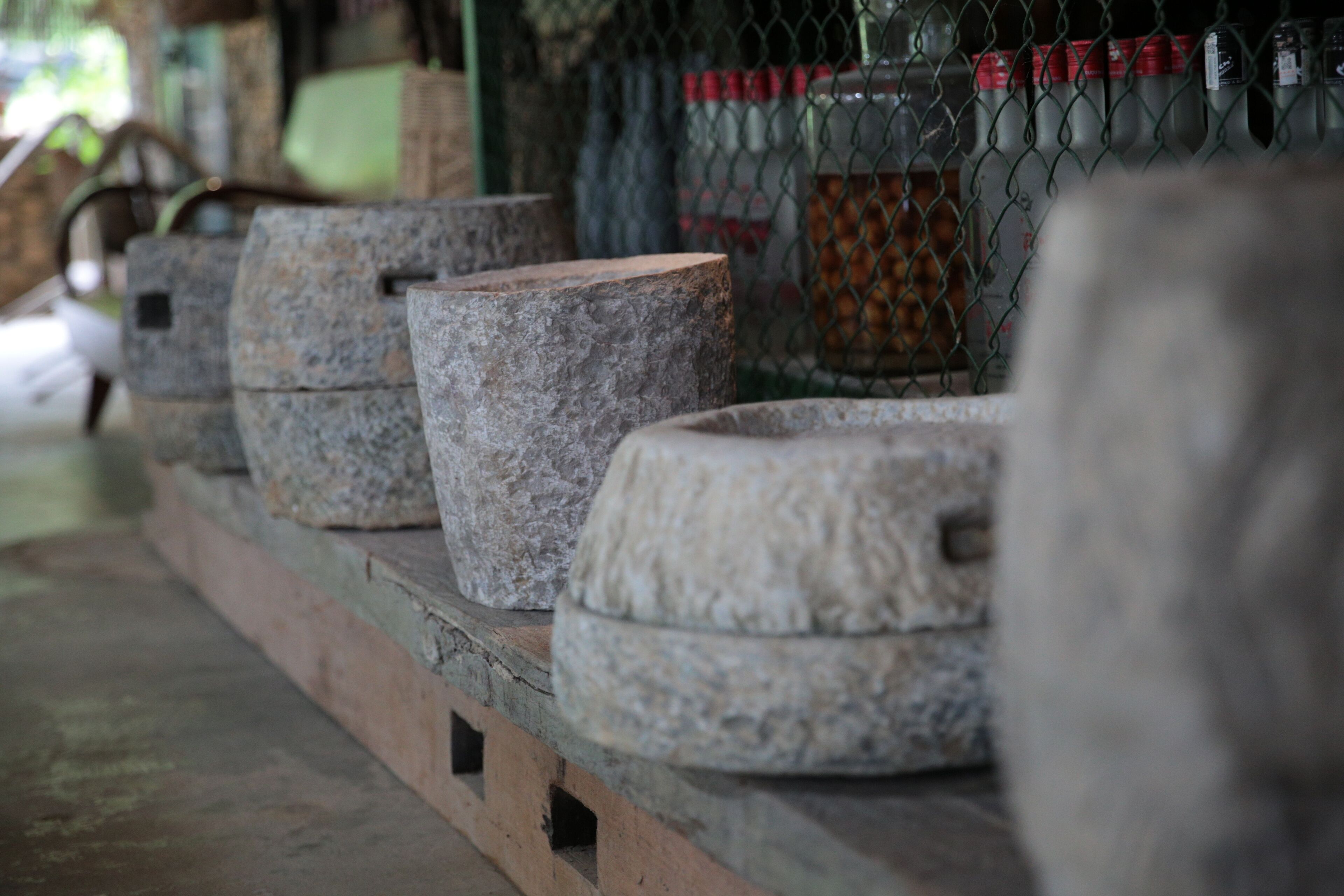 A row of stone basins lined up on a wooden platform, with a chain-link fence in the background.