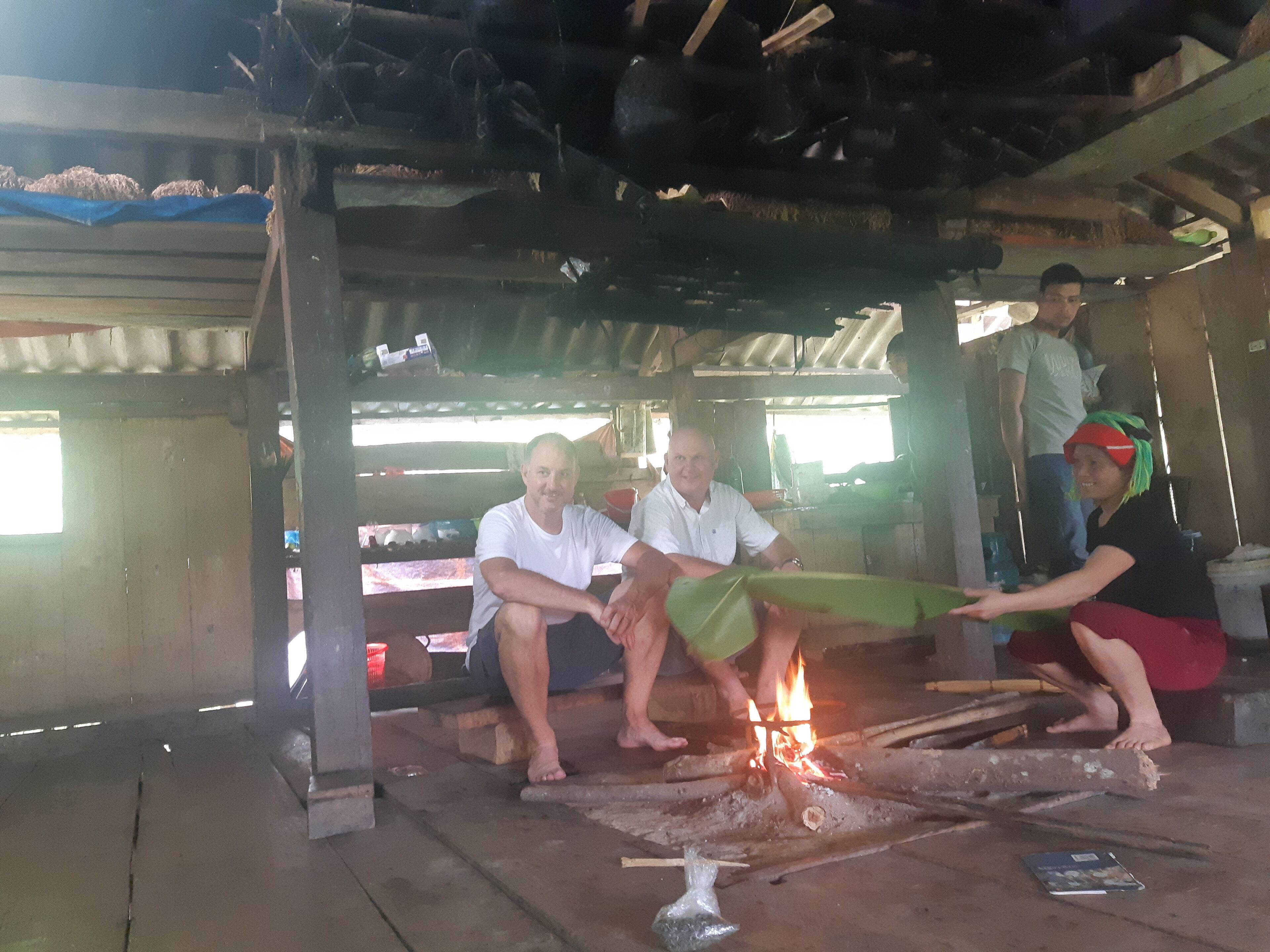 Un entorno rústico al aire libre con una fogata, bancos de madera y una estructura de refugio sencilla.
