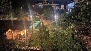 A nighttime view of a resort with a swimming pool, wooden deck, and surrounding greenery. - Historic Eco House & Ha Giang Loop (Ha Giang 2)