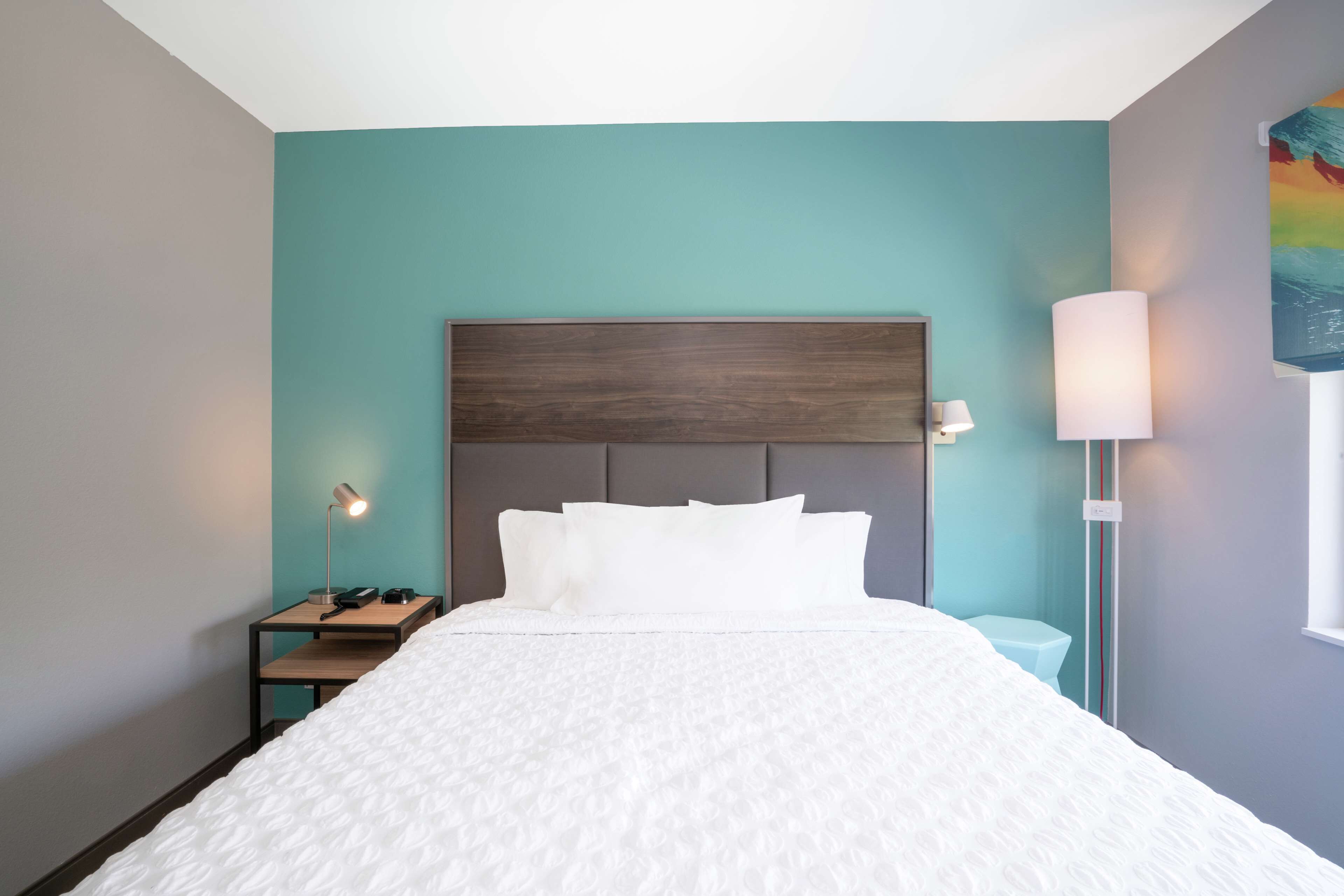 A neatly made bed in a room with teal walls, a wooden headboard, and a bedside table with a lamp.