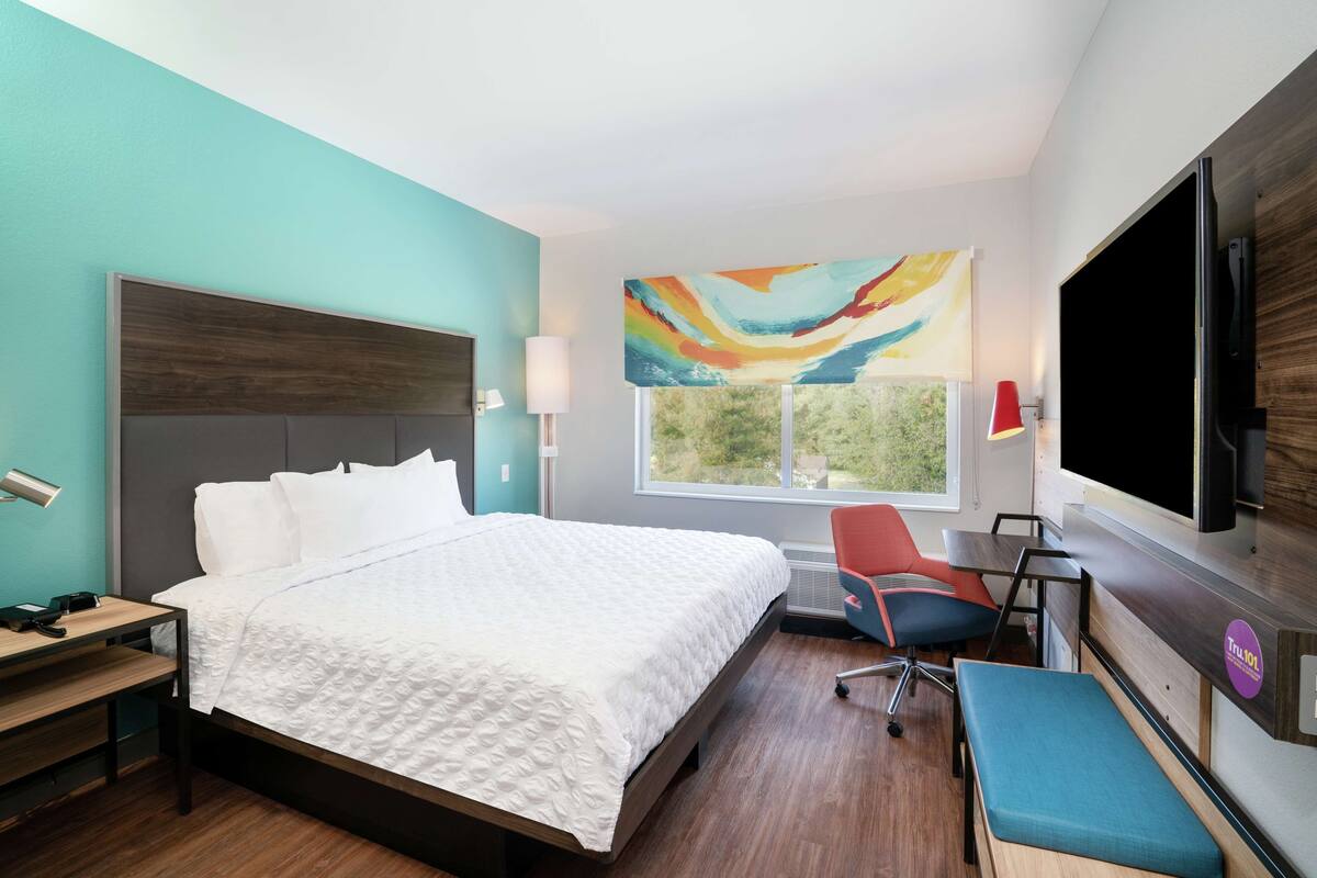 Habitación de hotel con una cama grande, un escritorio, una silla, un televisor y una ventana con vistas.