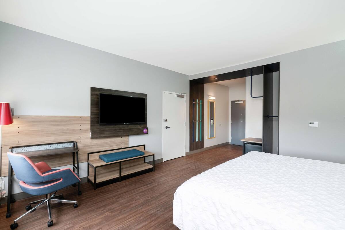 Una habitación de hotel moderna con una cama grande, un escritorio con silla, un televisor fijado a la pared y un baño visible a través de una puerta abierta.