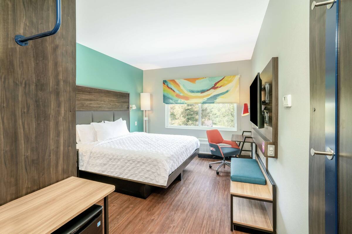 Habitación de hotel moderna con una cama grande, un escritorio, una silla, un televisor y una ventana con vistas.