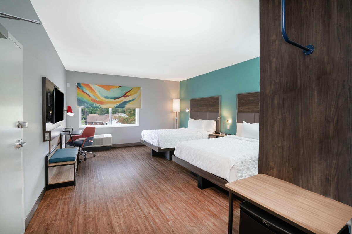 Une chambre d’hôtel avec deux lits, un bureau, une chaise, une télévision et une fenêtre donnant sur un beau paysage.