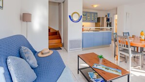 Een modern appartement met een blauwe bank, een houten eettafel en een keuken met blauwe keukenkastjes.