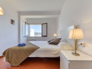 Une chambre d’hôtel avec un lit, une table de chevet avec une lampe, une fenêtre donnant sur un paysage dégagé et une petite table de chevet avec une lampe.