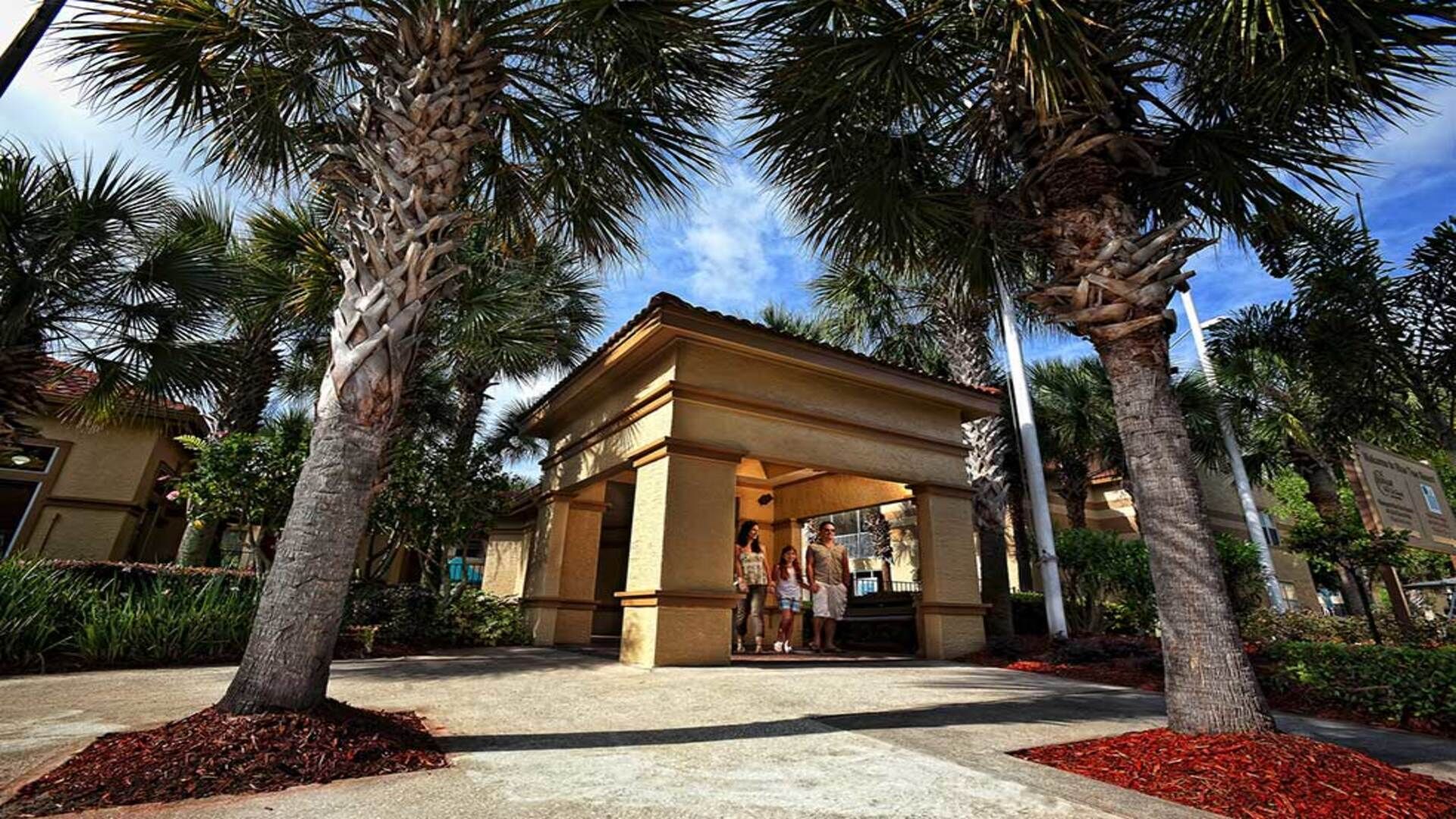 A covered outdoor area with palm trees, a building entrance, and a pathway.