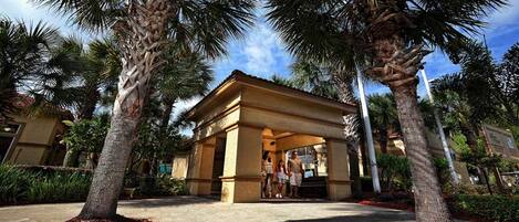 A covered outdoor area with palm trees, a building entrance, and a pathway.