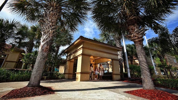 A covered outdoor area with palm trees, a building entrance, and a pathway.
