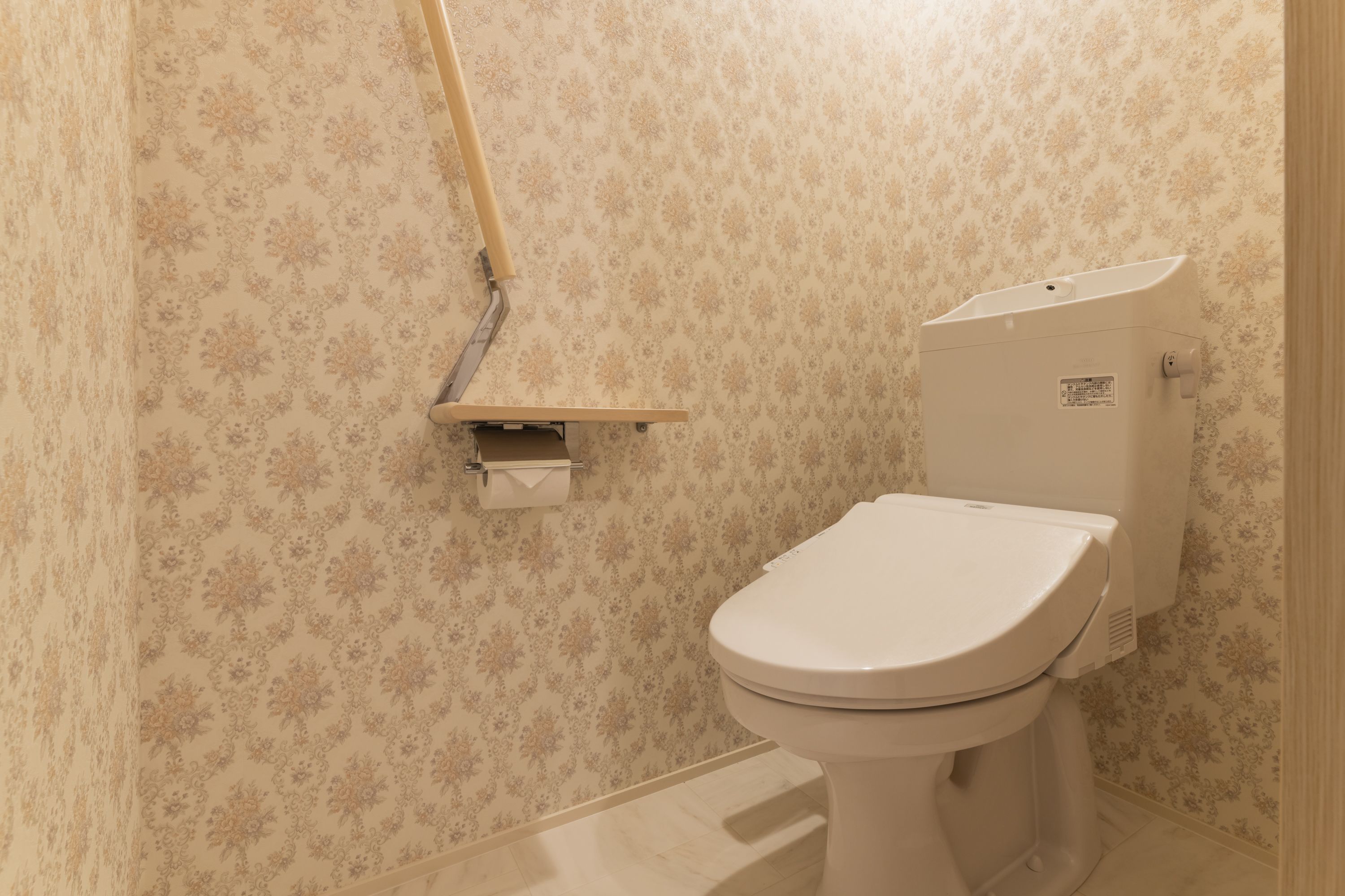 A bathroom with a toilet, a paper towel dispenser, and a wall-mounted shelf.