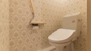 A bathroom with a toilet, a paper towel dispenser, and a wall-mounted shelf.