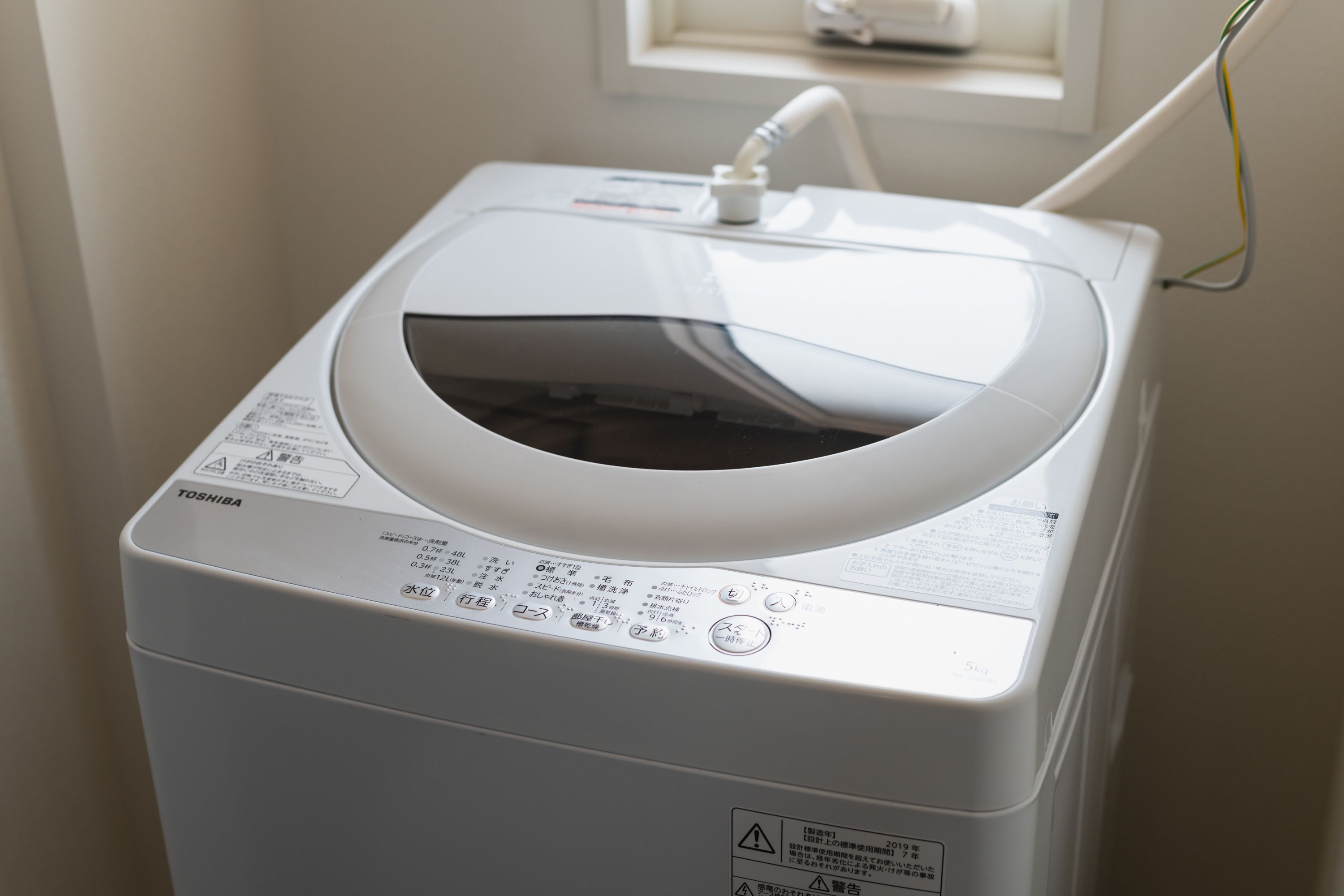 A white, front-loading washing machine with a control panel and a safety warning label.