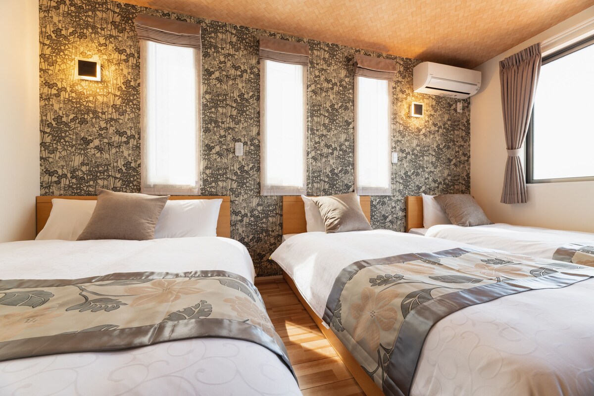 A hotel room with two beds, floral wallpaper, and a large window with curtains.
