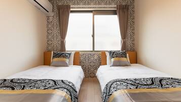 Habitación de hotel con dos camas, cortinas estampadas, un equipo de aire acondicionado y una ventana con vistas.
