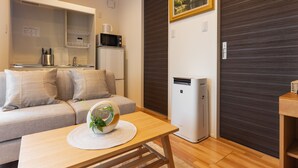 A modern living room with a sofa, a coffee table with a decorative bowl, a kitchen area with appliances, and a sliding door closet.