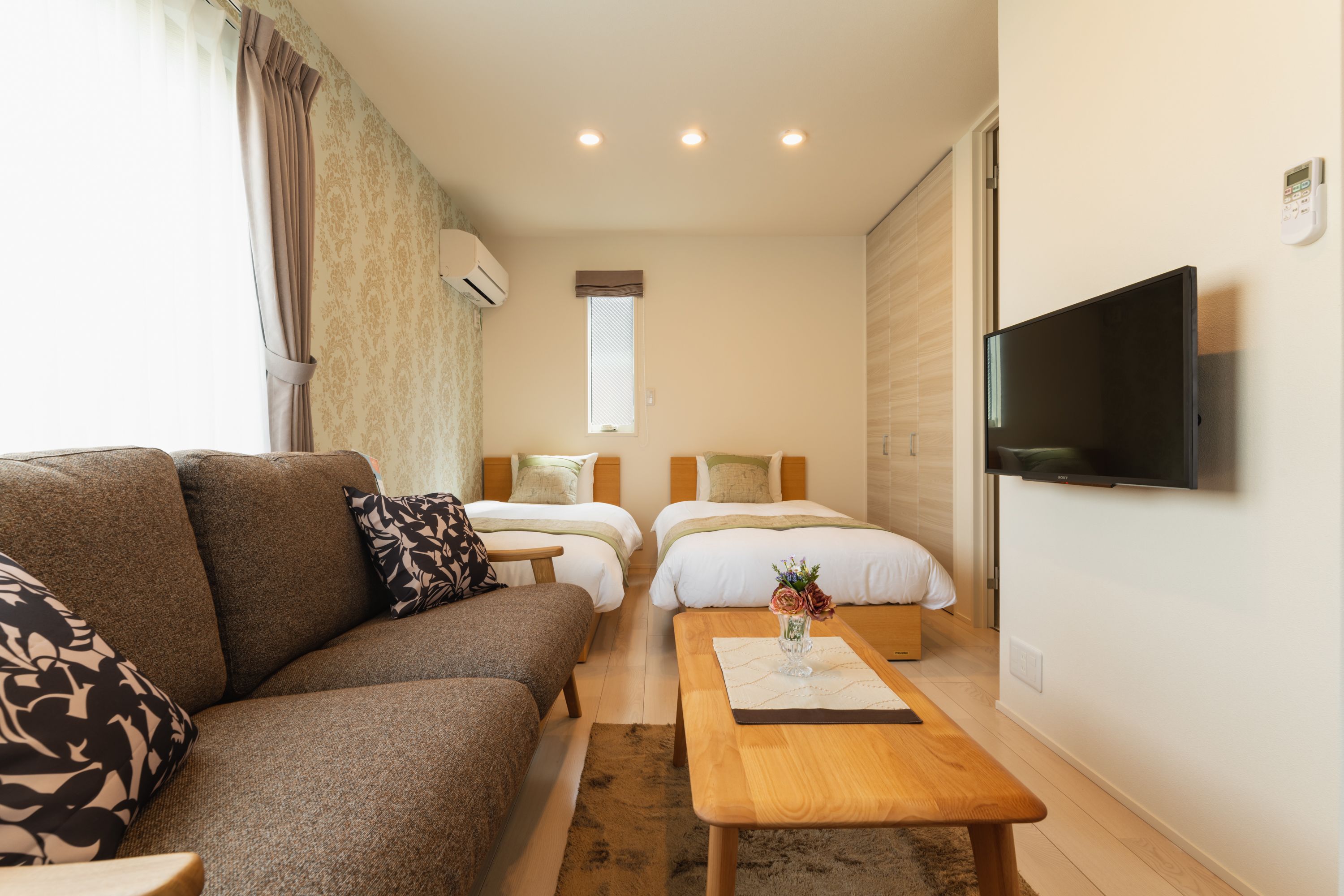 A hotel room with a sofa, two beds, a TV, and a small table with a vase.