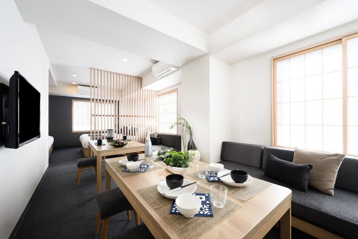 Un espace de repas moderne avec une longue table dressée pour le repas, un canapé et un téléviseur fixé au mur.