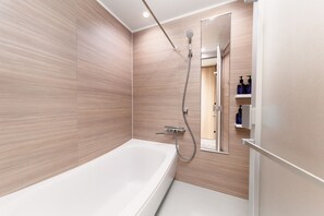 A modern bathroom with a large bathtub, a shower with a handheld showerhead, and a mirror above the sink. - MIMARU Tokyo Ueno Okachimachi (Tokyo)