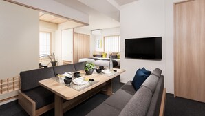 Una habitación de hotel moderna con zona de comedor, sofá, televisor y armario de madera.