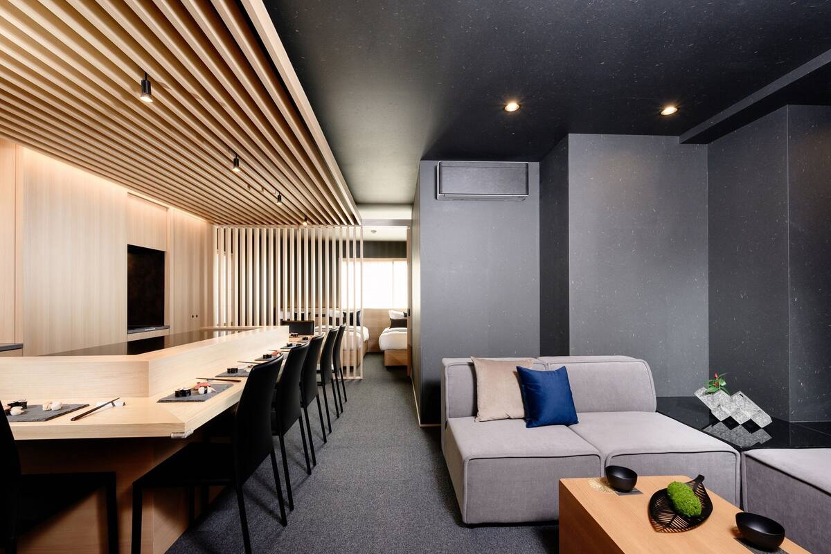 Une chambre d’hôtel moderne avec une longue table à manger, un canapé et une petite table basse en bois.