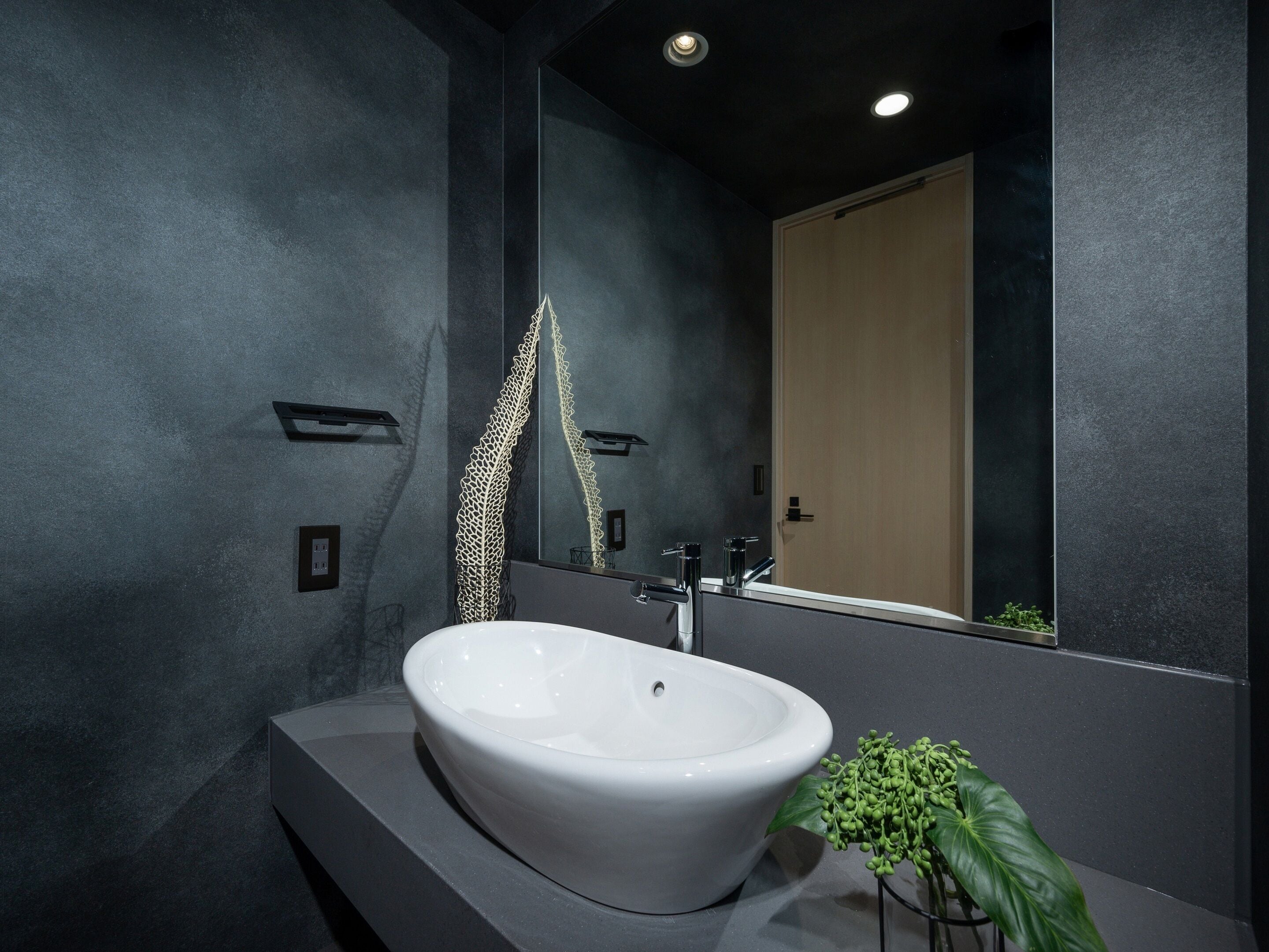 Un baño moderno con un lavabo blanco, paredes oscuras y un espejo grande.