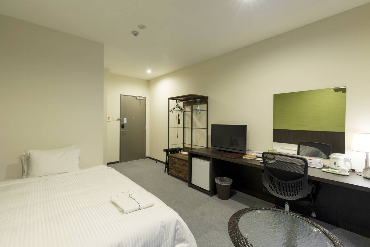 A hotel room with a bed, desk, chair, and a small table with a glass top.