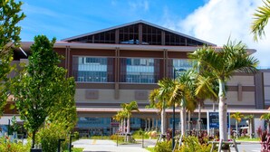 A modern building with a flat roof and large windows, surrounded by palm trees and other greenery. - Crown Hotel Okinawa Annex (Okinawa)
