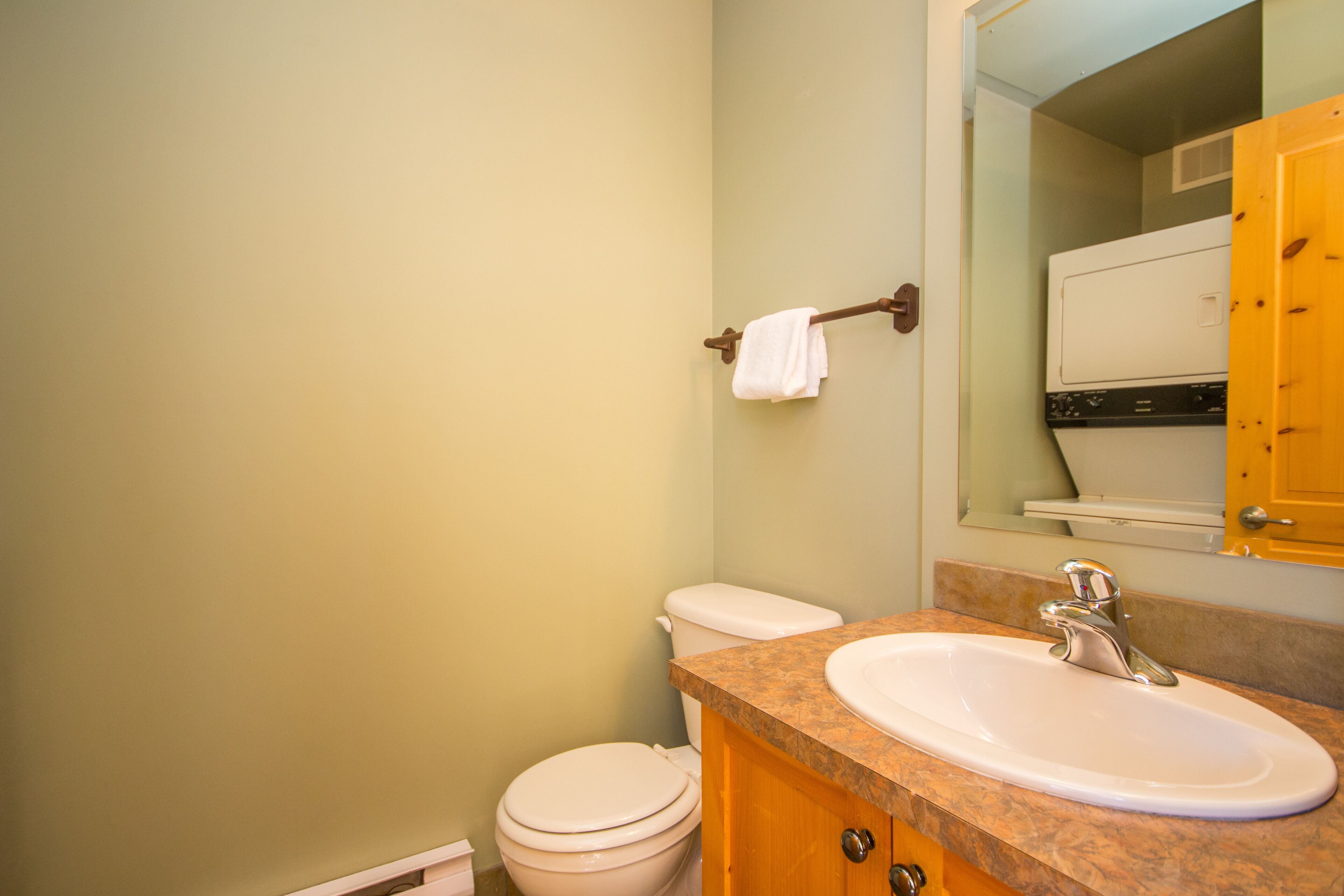 Un baño con inodoro blanco, lavamanos con encimera de mármol y mueble de madera.