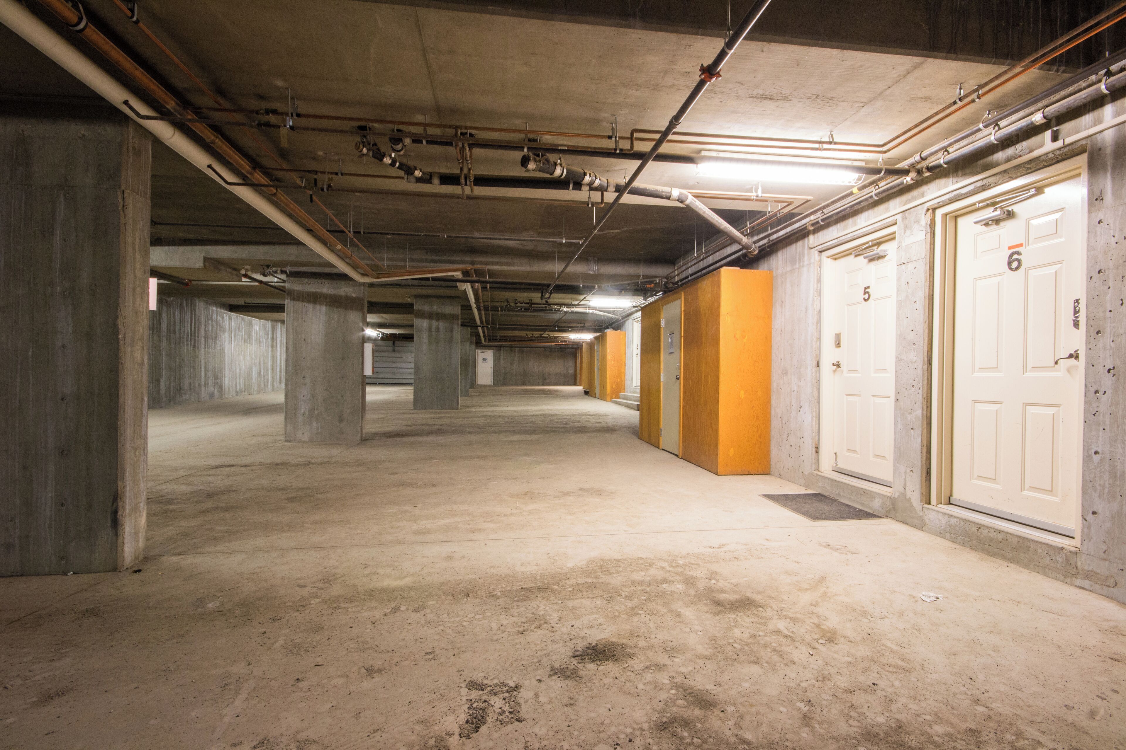 An underground parking garage with concrete pillars, fluorescent lighting, and numbered doors.