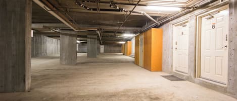 An underground parking garage with concrete pillars, fluorescent lighting, and numbered doors.