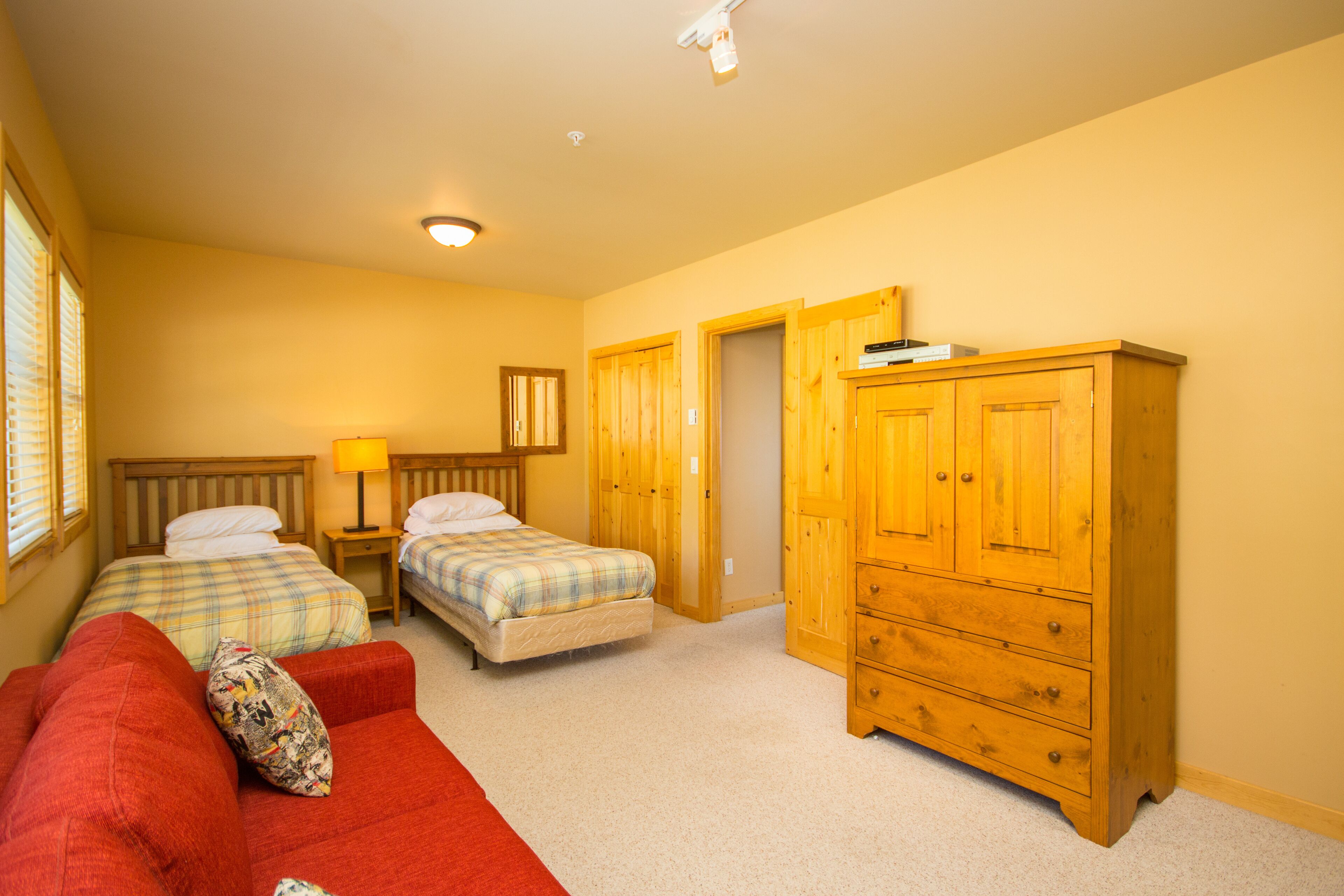 Een slaapkamer met twee bedden, een rode bank, een houten garderobe en een nachtkastje met een lamp.