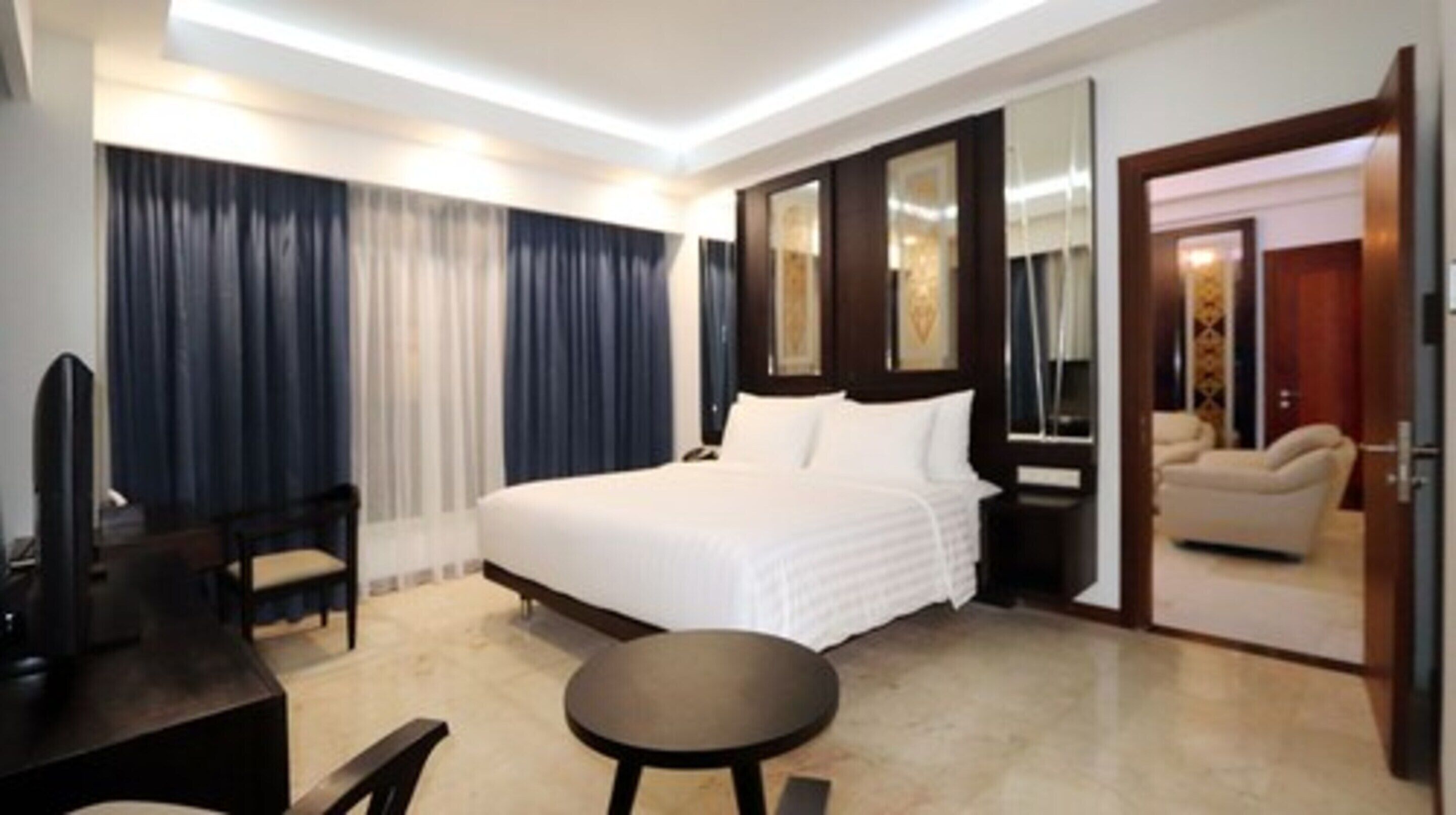 A hotel room with a large bed, a desk, a chair, and a small table.
